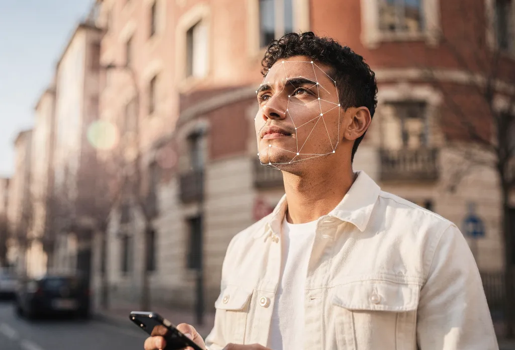 Young man with a facial-recognition mesh overlay holding a smartphone